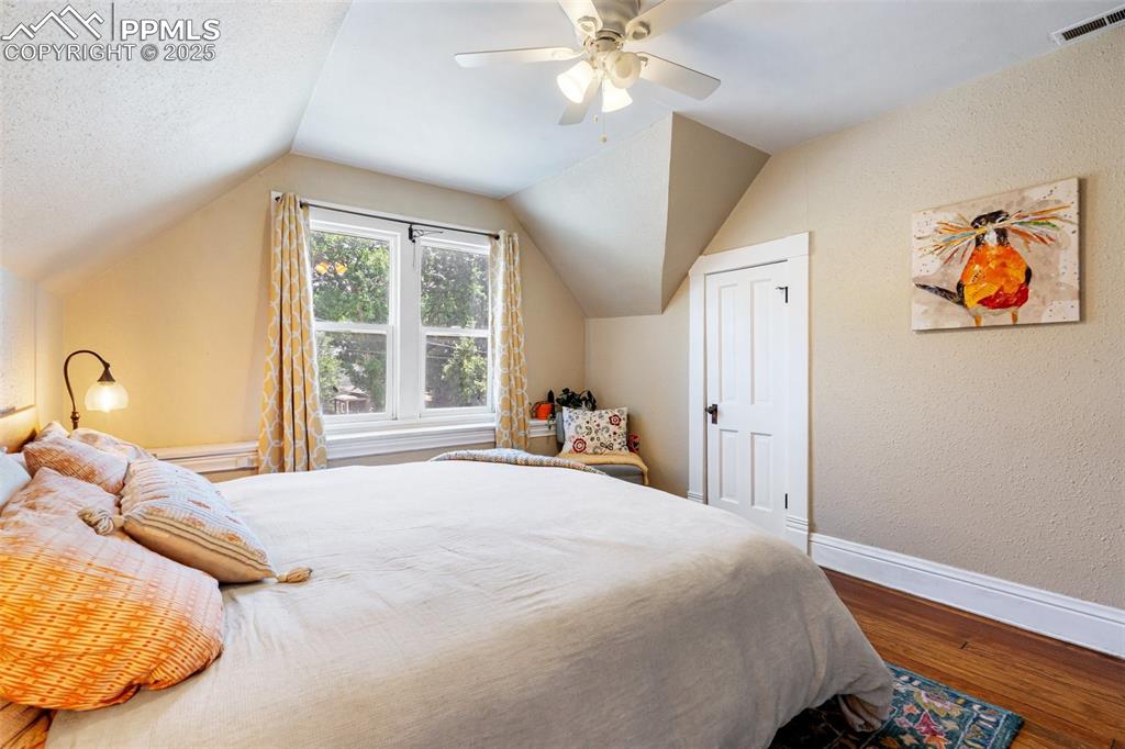 Bedroom featuring a textured wall, dark wood-type flooring, a ceiling fan, and vaulted ceiling