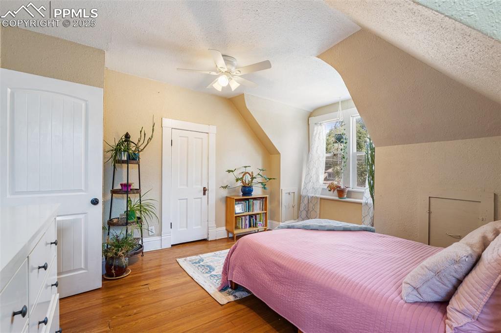 Bedroom with light wood-type flooring, a textured ceiling, vaulted ceiling, a ceiling fan, and a textured wall