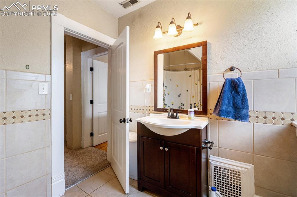 Bathroom featuring tile walls, a textured wall, vanity, light tile patterned floors, and curtained shower
