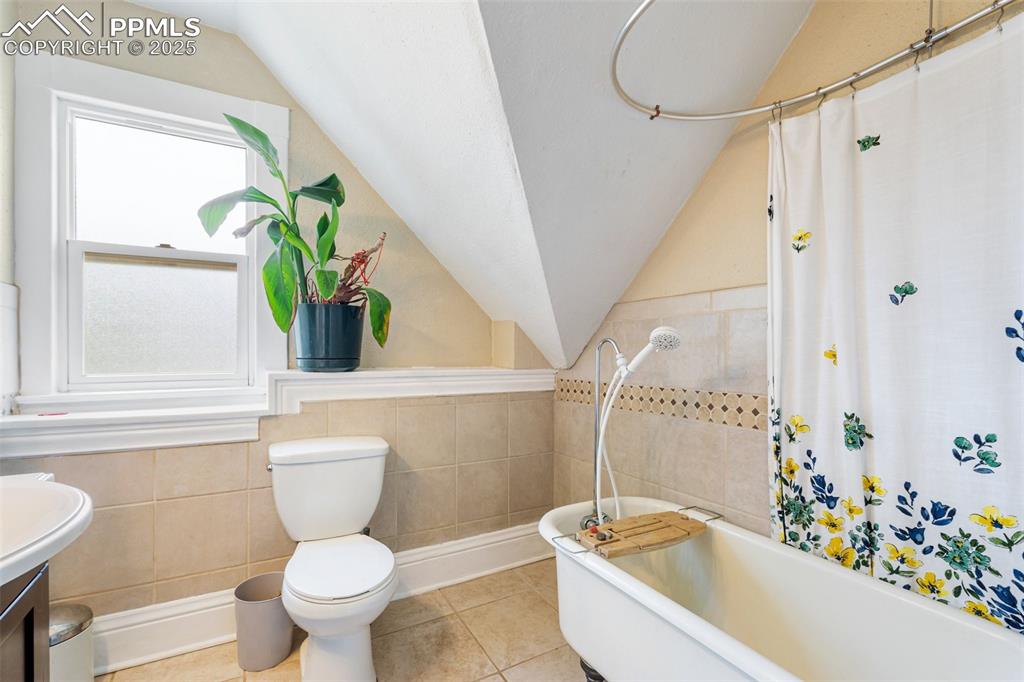 Full bathroom with tile walls, lofted ceiling, vanity, tile patterned flooring, and wainscoting