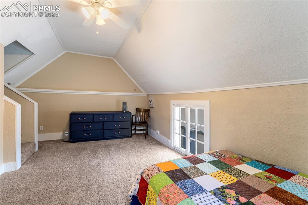 Bedroom featuring a textured wall, carpet floors, a ceiling fan, vaulted ceiling, and crown molding