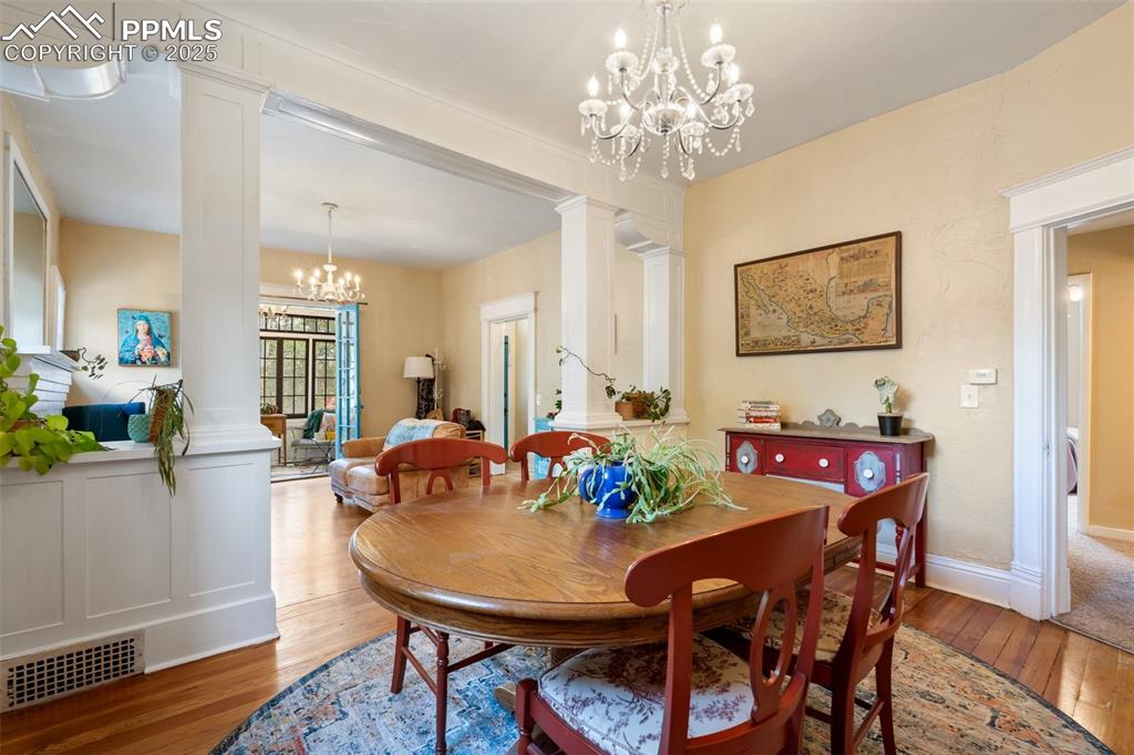 Dining room featuring ornate columns, a chandelier, and wood-type flooring
