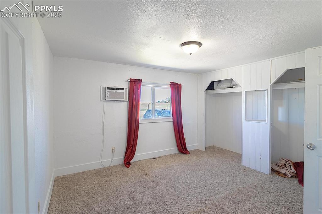 Unfurnished bedroom featuring a wall mounted AC, light colored carpet, a textured ceiling, a closet, and baseboards