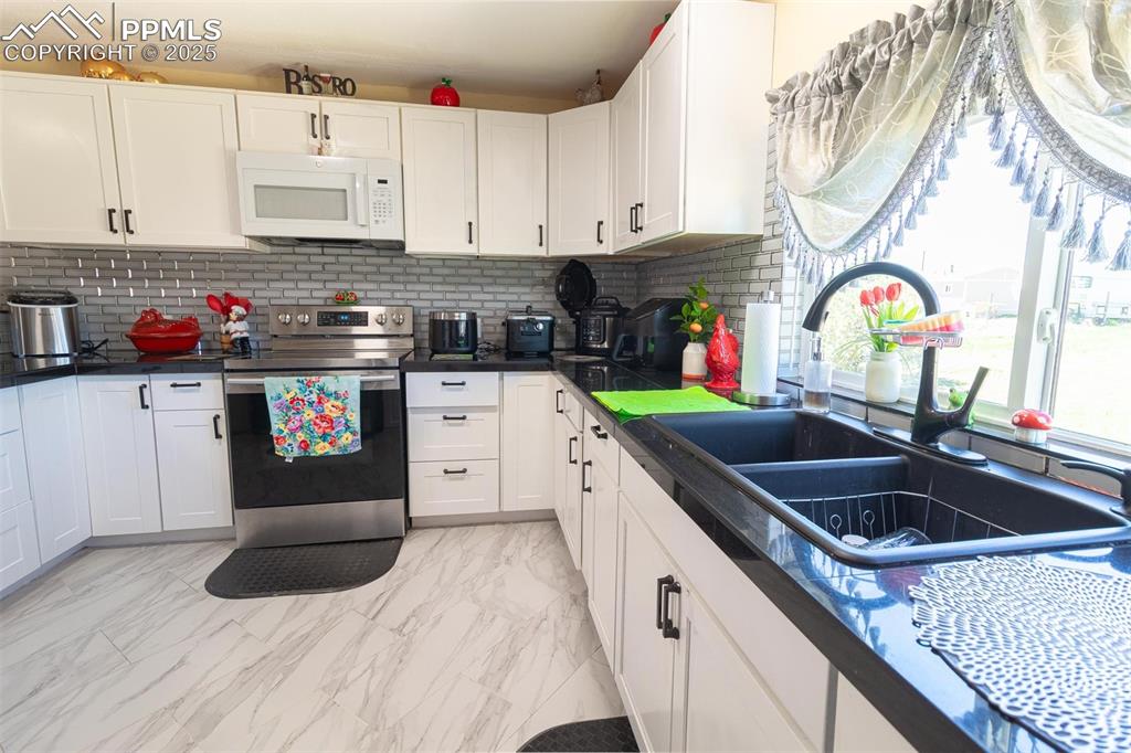 Kitchen featuring electric range, white microwave, a sink, dark countertops, and white cabinetry