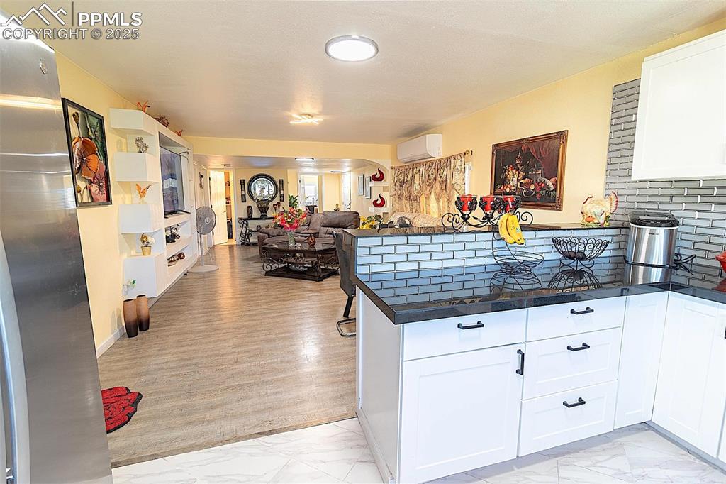 Kitchen featuring light marble finish floors, a peninsula, dark countertops, and white cabinetry