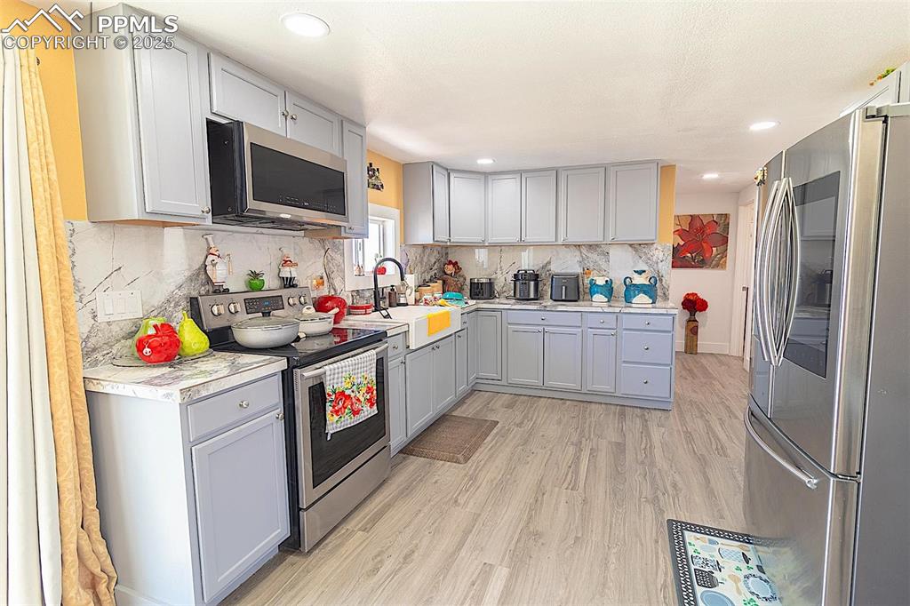Kitchen with stainless steel appliances, a sink, gray cabinetry, light wood finished floors, and light countertops