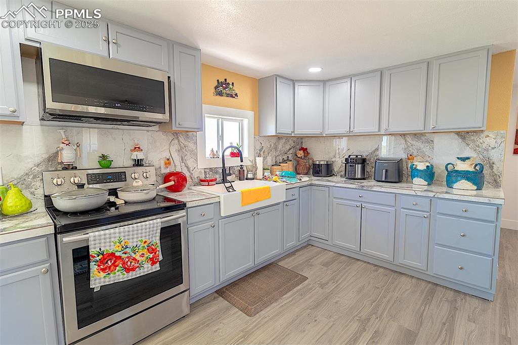 Kitchen featuring appliances with stainless steel finishes, a sink, light wood finished floors, light countertops, and tasteful backsplash