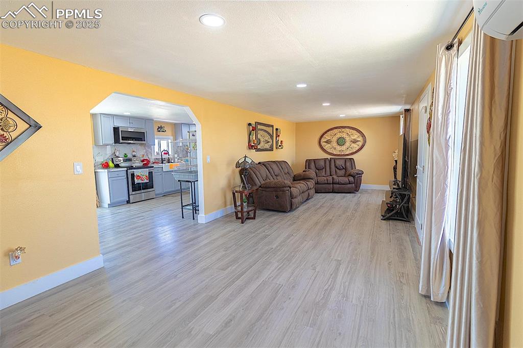 Living area with light wood-style flooring, arched walkways, baseboards, a wall mounted AC, and recessed lighting