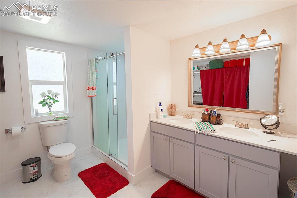 Full bathroom with marble finish floors, a shower stall, double vanity, toilet, and baseboards