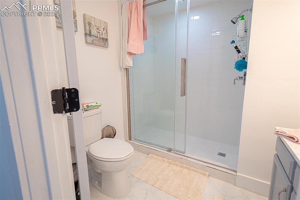 Full bathroom with toilet, marble finish floors, vanity, a shower stall, and baseboards