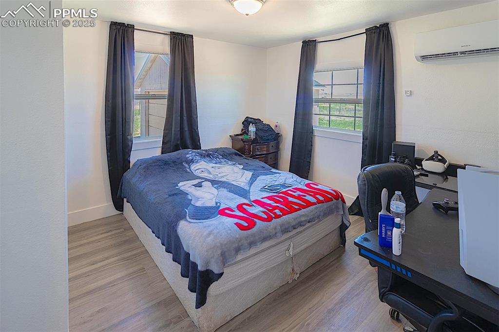 Bedroom featuring a wall mounted air conditioner, wood finished floors, and baseboards