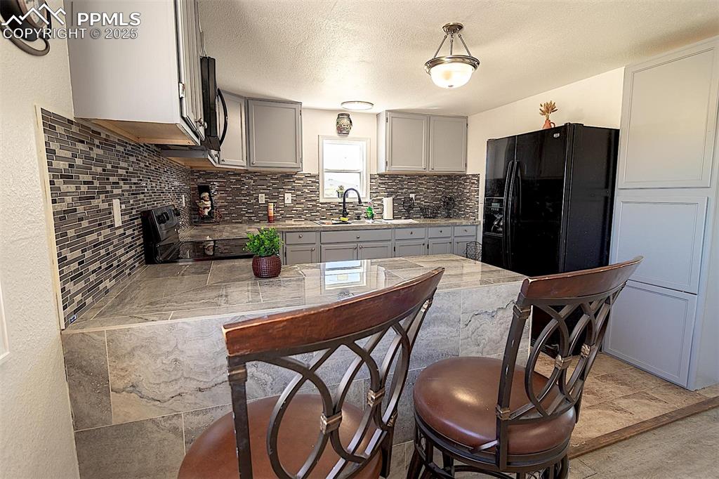 Kitchen featuring black appliances, a sink, decorative backsplash, light countertops, and gray cabinetry