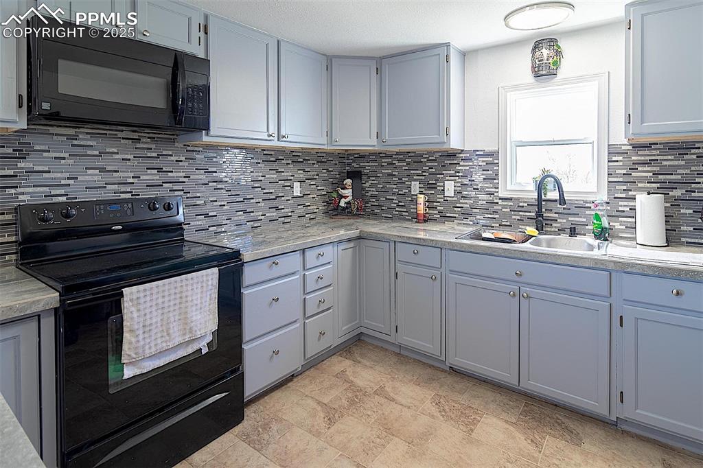 Kitchen with black appliances, a sink, decorative backsplash, and light countertops