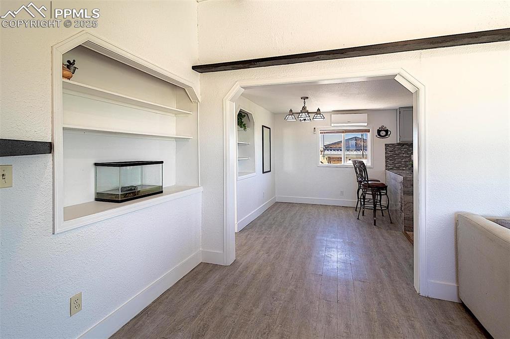 Dining area with baseboards, wood finished floors, a wall mounted AC, a chandelier, and built in shelves