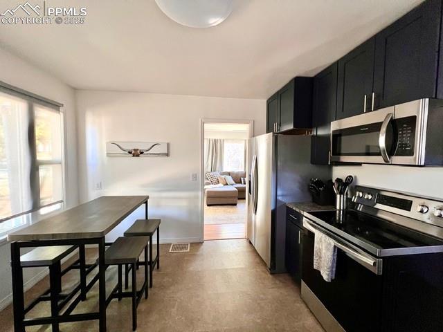 Kitchen featuring dark cabinets, appliances with stainless steel finishes, and light floors