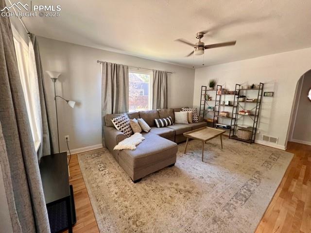 Living room featuring arched walkways, light wood flooring, ceiling fan, and a textured ceiling