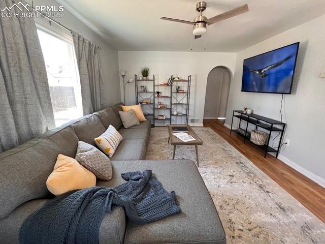Living room featuring wood floors, arched walkways, a textured wall, and a ceiling fan