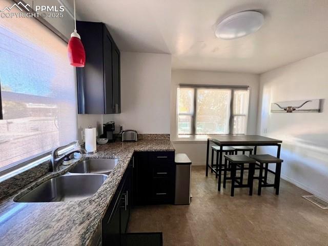 Kitchen featuring stone countertops, pendant lighting, and dark cabinetry