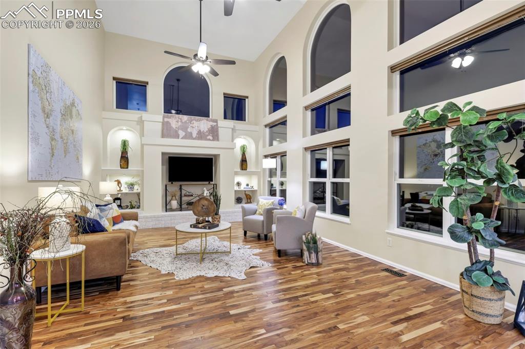 Living area with a ceiling fan, built in shelves, a fireplace with raised hearth, wood finished floors, and a high ceiling