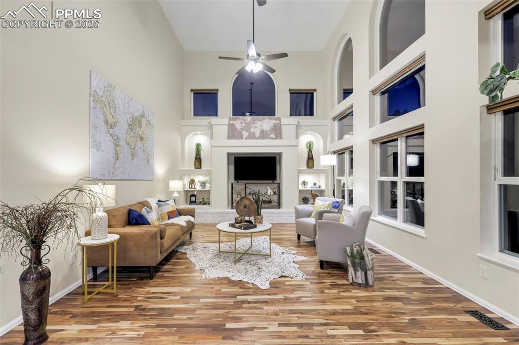 Living area featuring built in features, a high ceiling, a ceiling fan, a brick fireplace, and wood finished floors