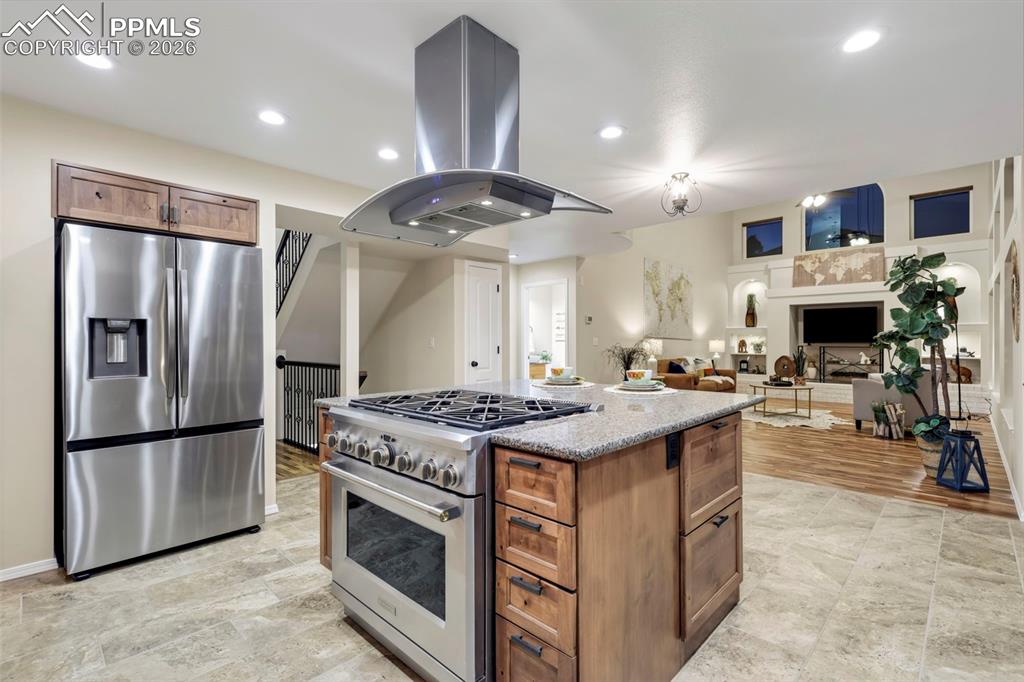 Kitchen with wood finish cabinets, stainless steel appliances, island exhaust hood, a center island, and light stone countertops