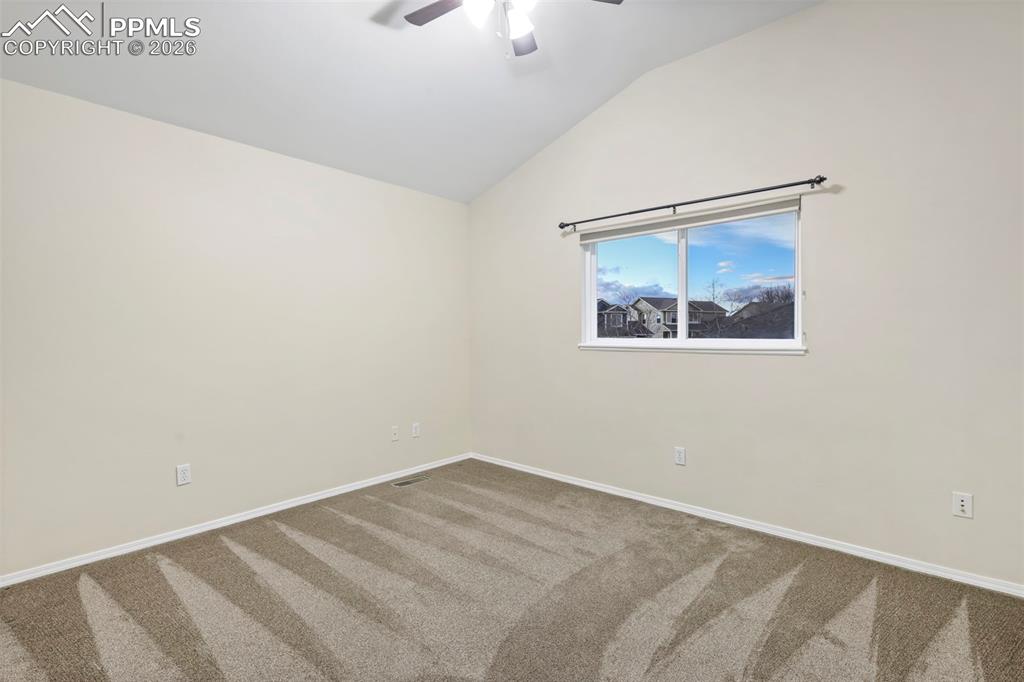 Carpeted spare room featuring vaulted ceiling and ceiling fan