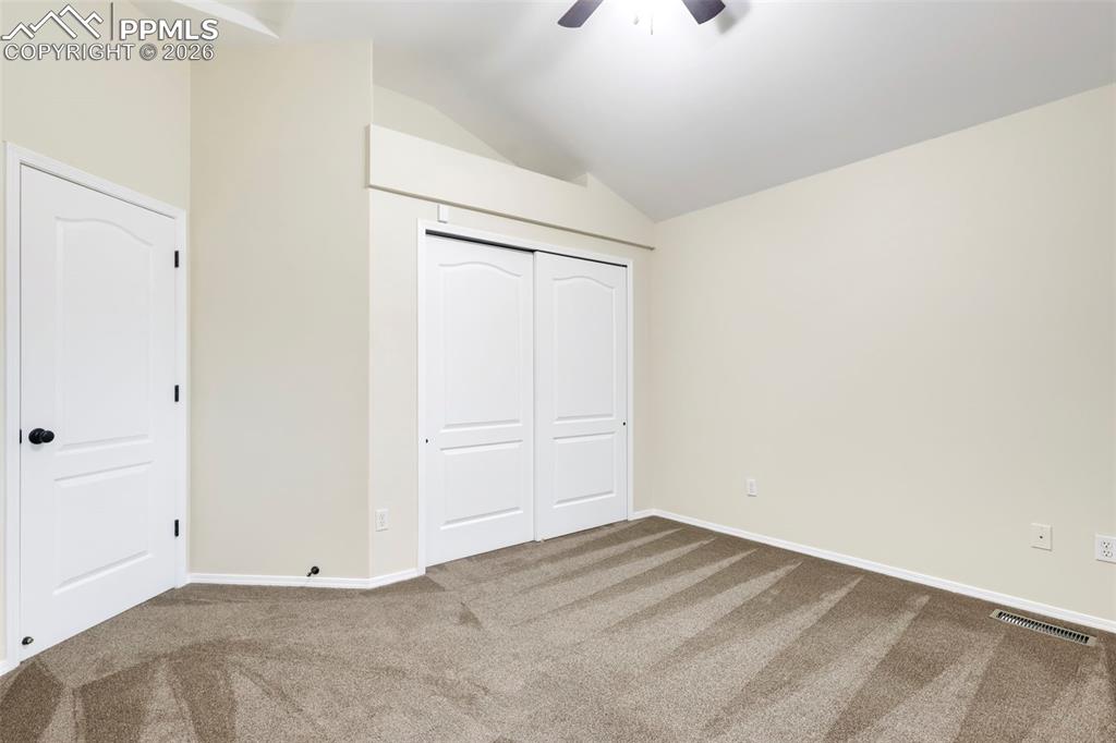 Unfurnished bedroom featuring vaulted ceiling, carpet, a closet, and a ceiling fan