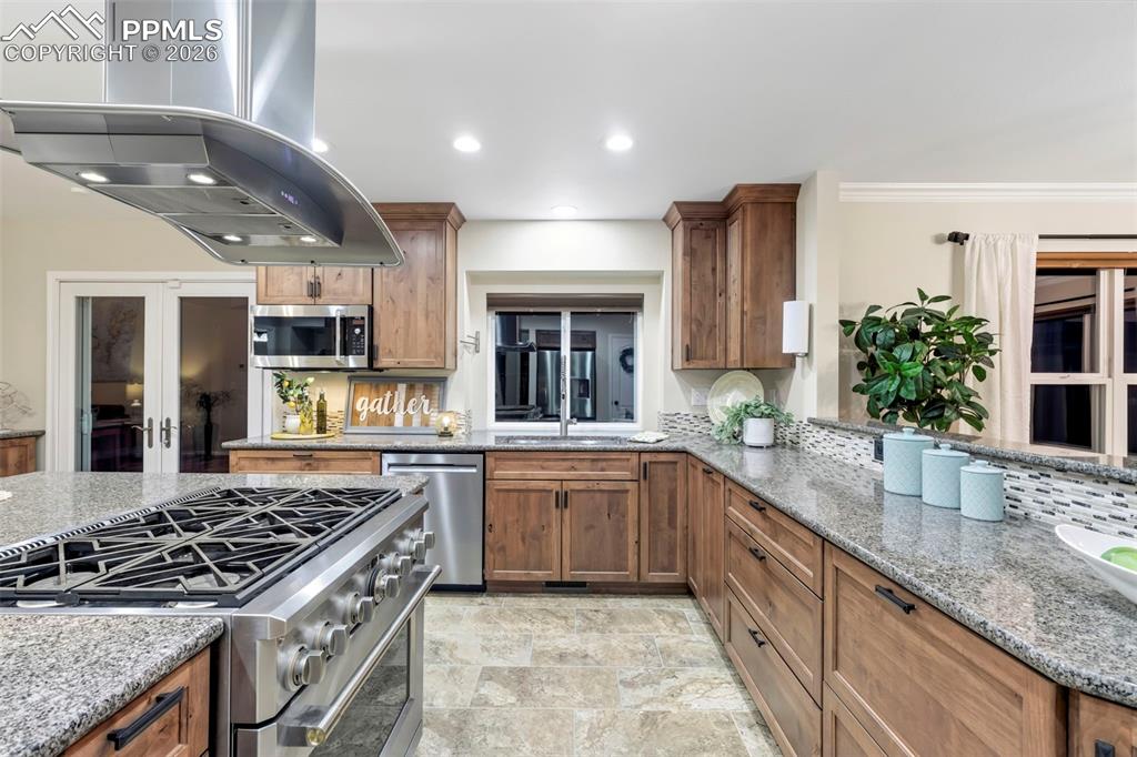 Kitchen featuring stainless steel appliances, island range hood, light stone countertops, wood finish cabinets, and recessed lighting