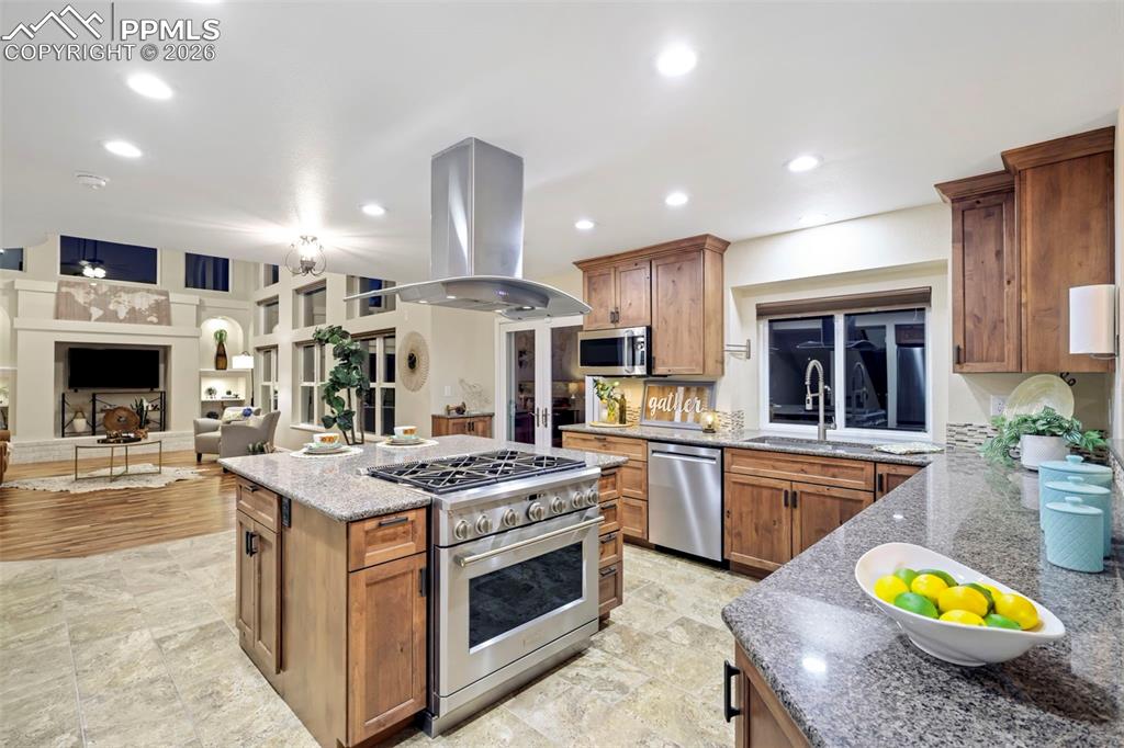 Kitchen with light stone counters, stainless steel appliances, wood finish cabinetry, island range hood, and recessed lighting