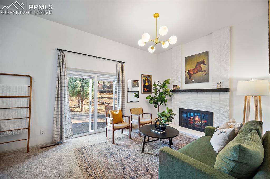 Living area with a white brick fireplace, light carpet, and a chandelier