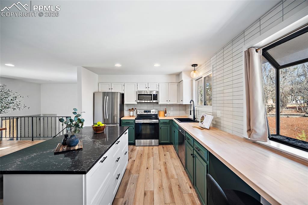 Two tone kitchen featuring dual tone cabinets, stainless steel appliances, light wood finished floors, healthy amount of natural light, and backsplash
