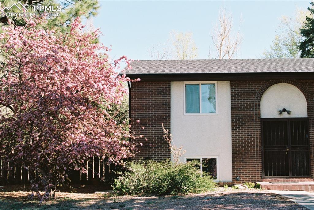 Film photo of the home in the spring. View of side of home with brick siding, stucco siding, and a shingled roof