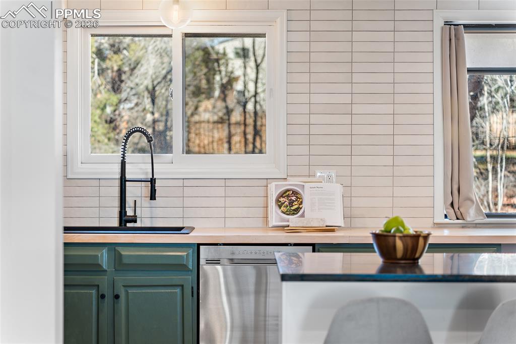 Kitchen featuring green cabinets, stainless steel dishwasher, and backsplash
