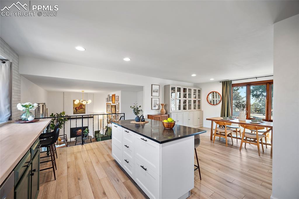 Kitchen featuring two breakfast bar areas, two tone cabinetry, light wood-style flooring, dark stone countertops, and hanging lights