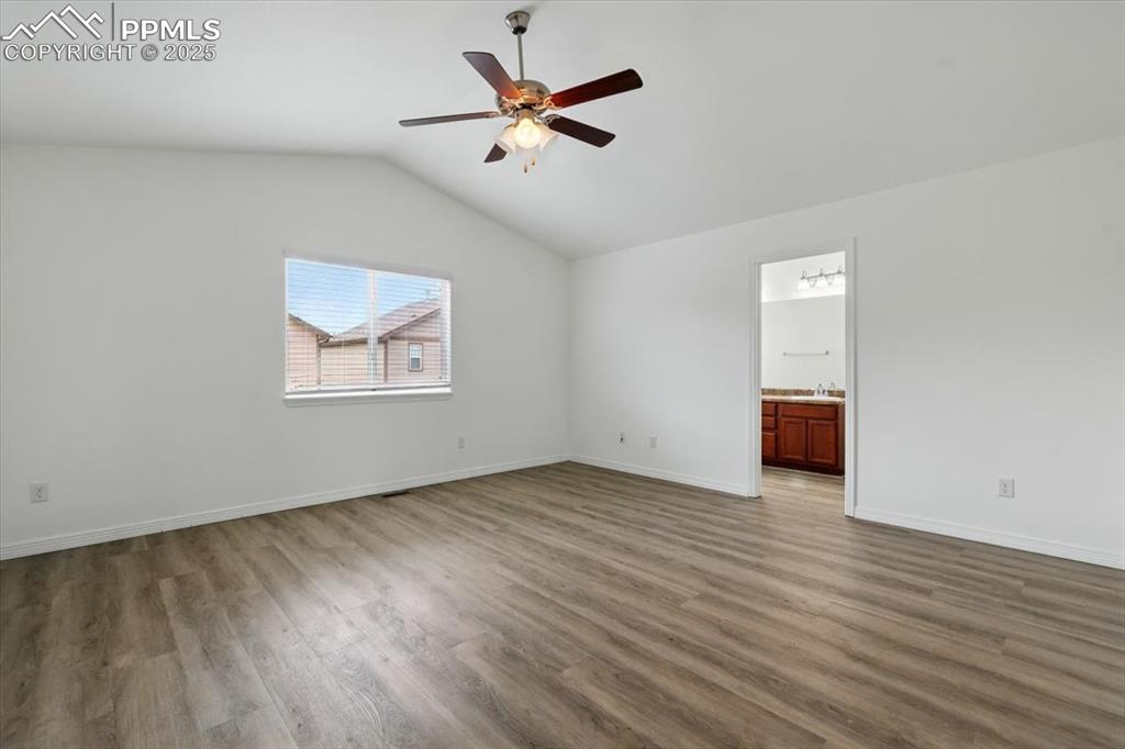 Unfurnished room featuring wood finished floors, vaulted ceiling, a ceiling fan, a sink, and baseboards