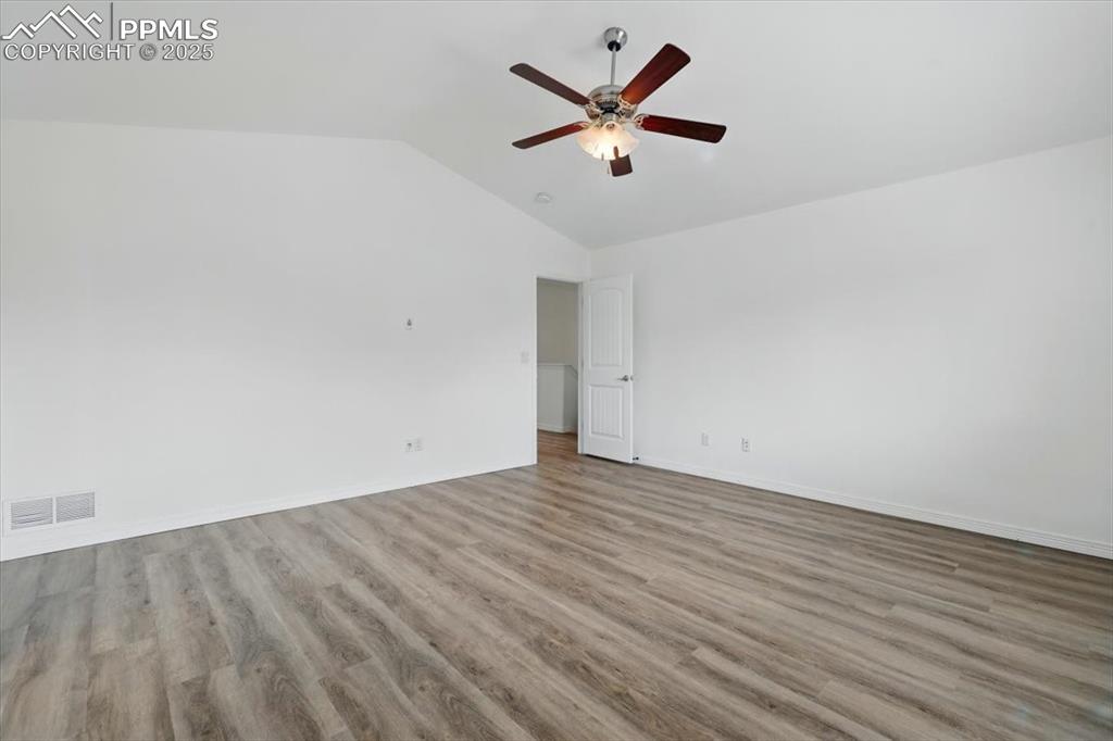 Spare room featuring a ceiling fan, vaulted ceiling, wood finished floors, and baseboards