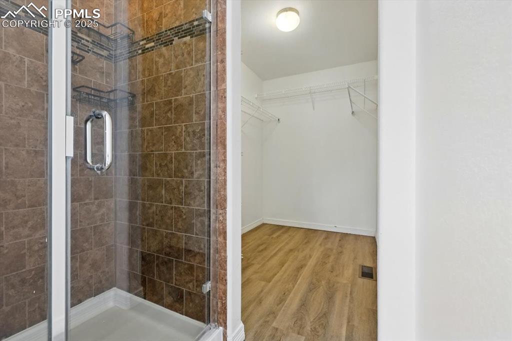 Bathroom featuring a stall shower, wood finished floors, a spacious closet, and baseboards
