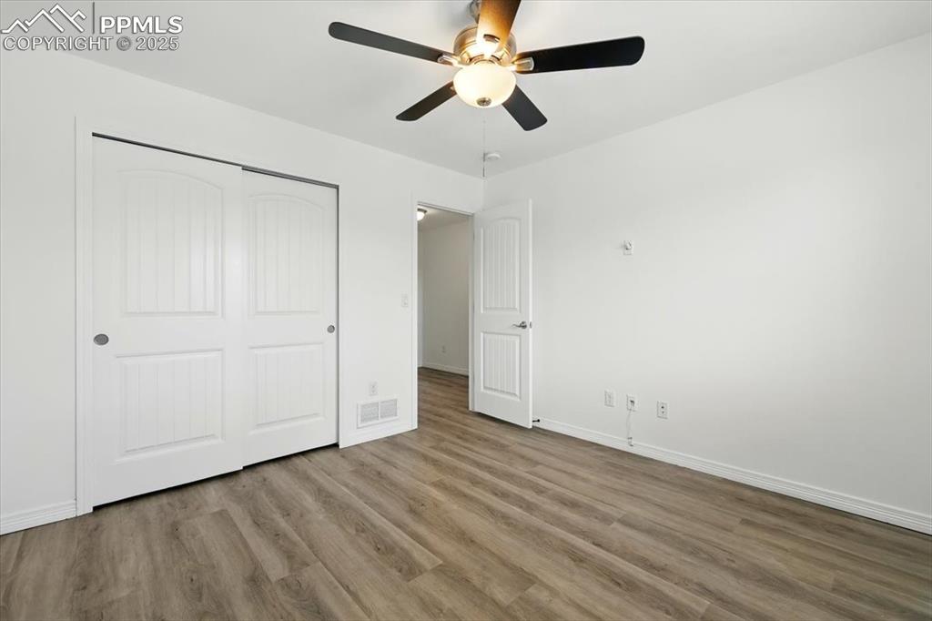 Unfurnished bedroom featuring wood finished floors, a closet, baseboards, and a ceiling fan