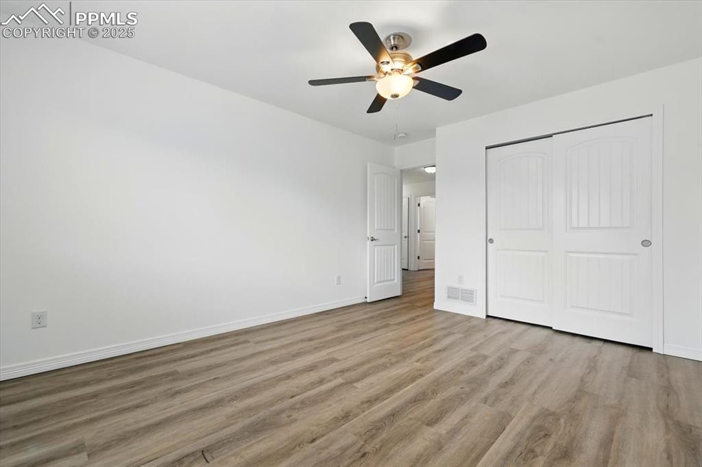 Unfurnished bedroom featuring wood finished floors, baseboards, a closet, and a ceiling fan