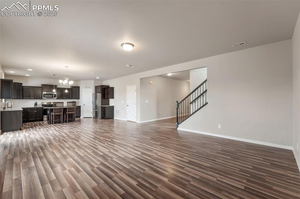 Unfurnished living room featuring suspended lighting and dark wood finished floors