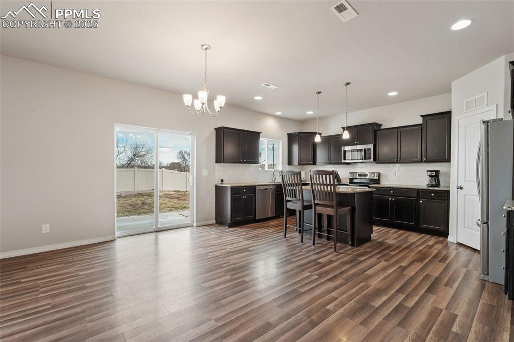 Kitchen with a kitchen breakfast bar, backsplash, stainless steel appliances, hanging lights, and a kitchen island