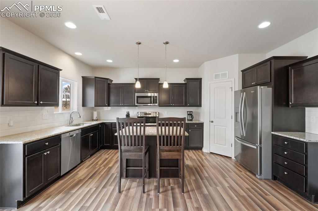 Kitchen with decorative light fixtures, backsplash, stainless steel appliances, dark wood finish cabinetry, and a breakfast bar area