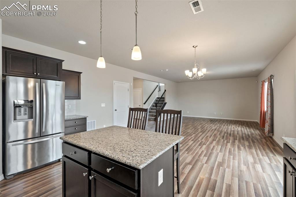 Kitchen with stainless steel fridge with ice dispenser, light stone counters, dark wood finished floors, a center island, and open floor plan