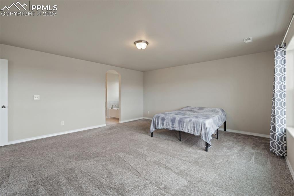 Carpeted bedroom featuring arched walkways and connected bathroom