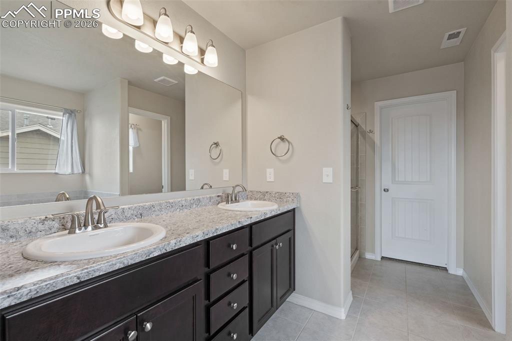 Bathroom with double vanity, a stall shower, and light tile patterned flooring