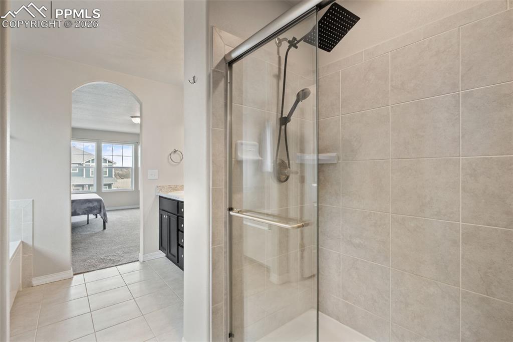 Ensuite bathroom featuring vanity, a shower stall, light tile patterned floors, and light carpet