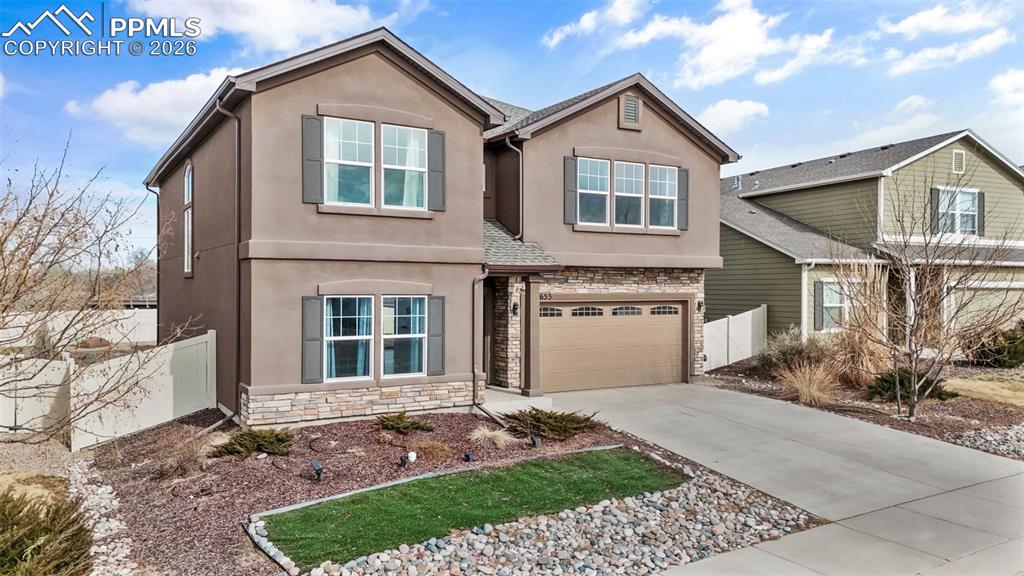 View of front of home with stone siding, stucco siding, a garage, and concrete driveway