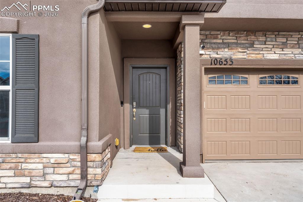 Property entrance with stone siding, a garage, and driveway