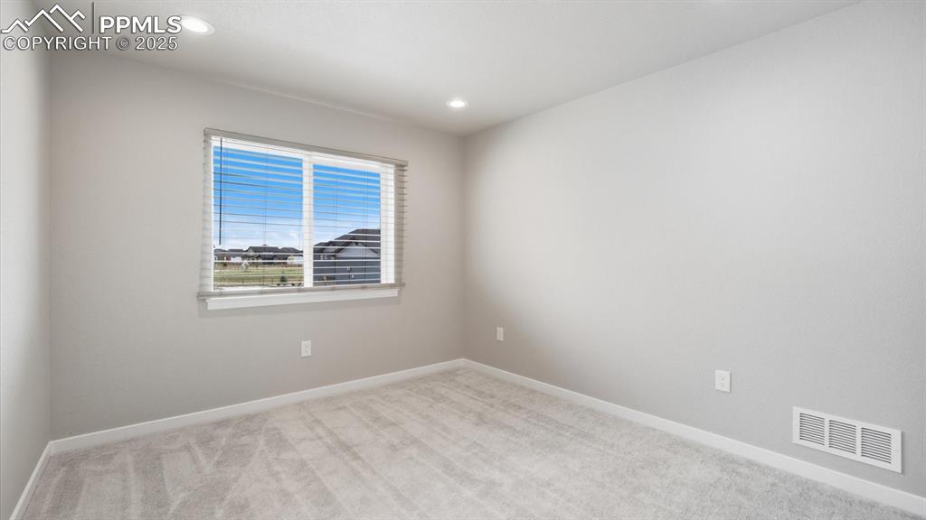 Bedroom #2 with neutral carpet and front view window.