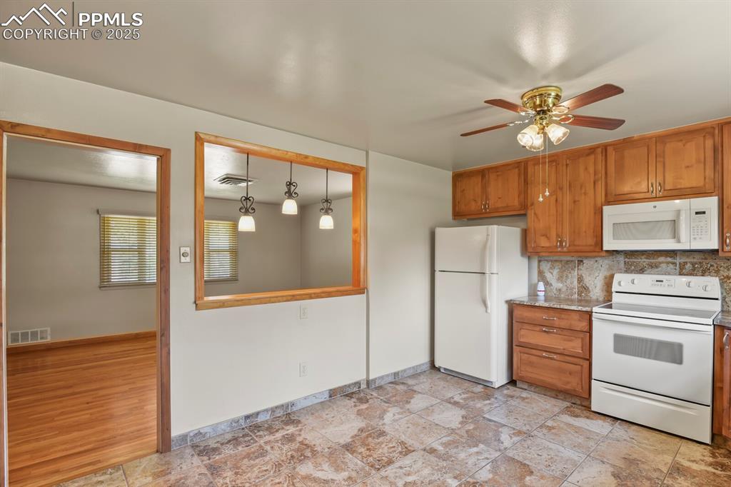 Kitchen with white appliances, brown cabinetry, a ceiling fan, and tasteful backsplash